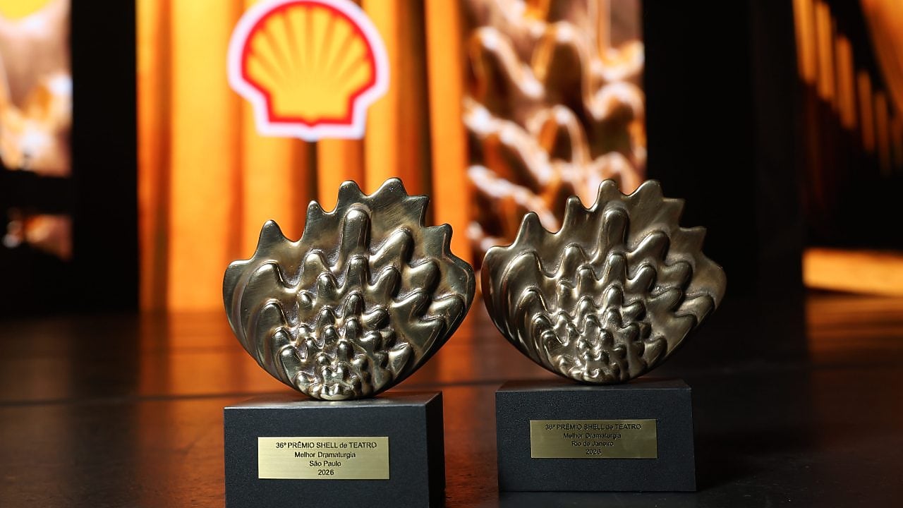 Dois troféus dourados do 35º Prêmio Shell de Teatro sobre um palco, com o logo da Shell ao fundo em cenário amarelo.