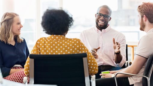 Grupo diverso de pessoas reunidas em um ambiente profissional, com diferentes gêneros, etnias e estilos, sentadas em círculo durante uma conversa colaborativa. A cena transmite inclusão e pluralidade, com participação equilibrada e escuta ativa entre os integrantes, reforçando a ideia de troca de perspectivas e convivência em um espaço de trabalho diverso.