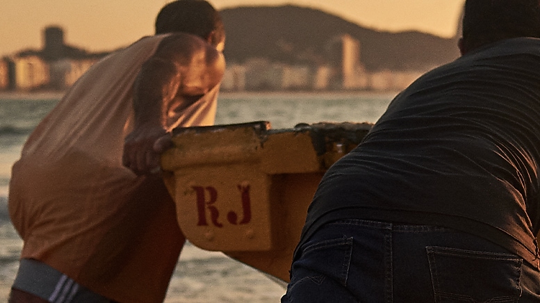 No centro da imagem temos um grupo de pescadores empurrando um barco em direção ao mar