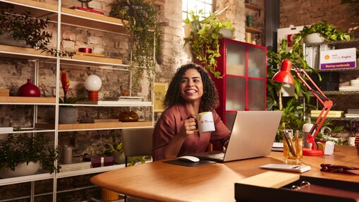 Mulher negra segurando caneca em frente ao seu computador em sala toda decorada com plantas
