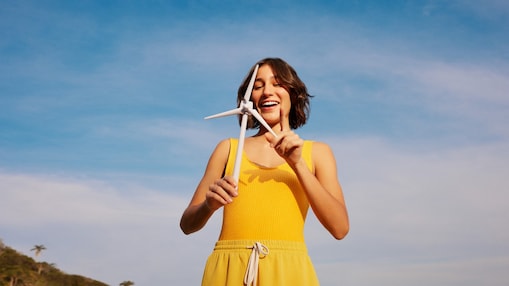 Na imagem, uma menina com roupa amarela segura uma miniatura de um aerogerador de energia eólica