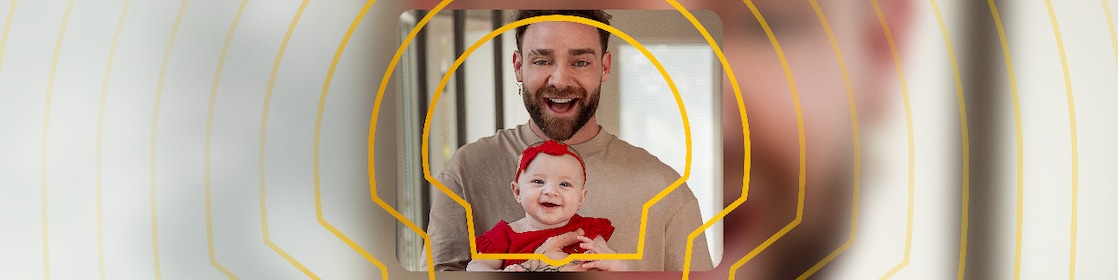 O influenciador Zanq segura sua bebê, que veste uma roupa vermelha.