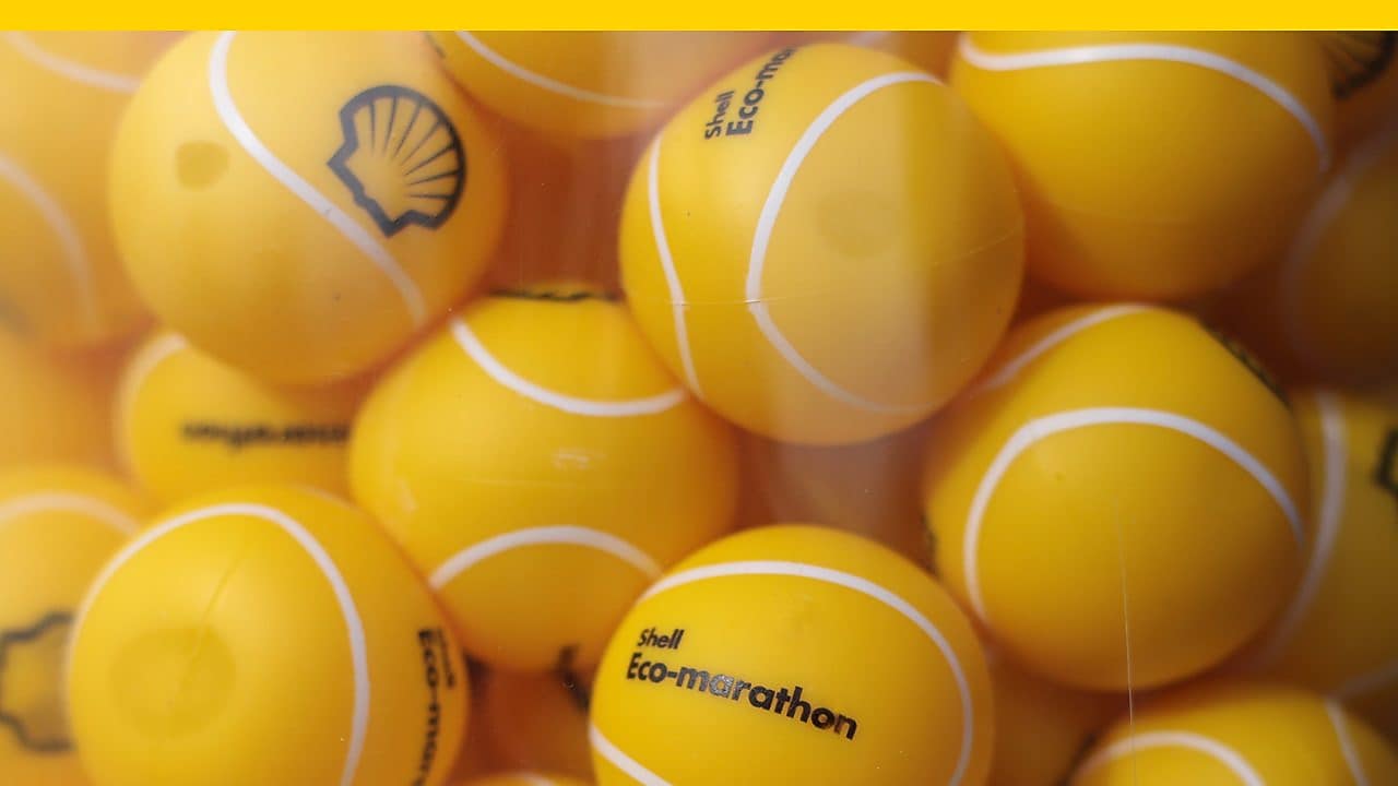 Vemos na foto um amontoado de bolinhas amarelas de tênis. Em algumas, vemos o logo da Shell preto. Em outras, podemos ler em fonte preta o texto: “Shell Eco-marathon”.