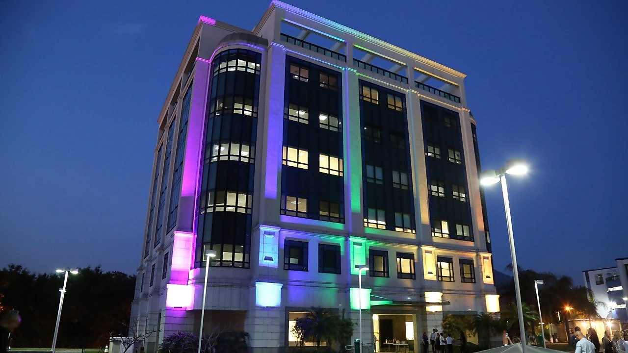 Na imagem, é possível ver um prédio, de cerca de 6 andares, iluminado com as cores da bandeira do arco-íris: vermelho , laranja, amarelo, verde, azul e roxo.