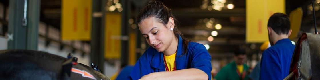 Em um fundo amarelo, vemos três ilustrações de mulheres com uniforme da Shell posicionadas lado a lado. A primeira está com um jaleco vermelho e fones de proteção, a segunda com o uniforme branco e a terceira com uniforme vermelho, fone de proteção e capacete de proteção branco.