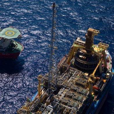 Vista aérea de duas embarcações offshore no oceano, uma delas equipada com heliponto e a outra com extensa estrutura industrial, tubulações, equipamentos e uma torre central.