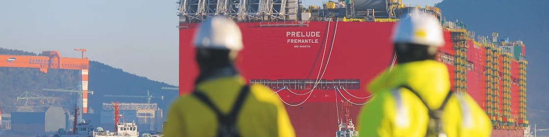 Funcionários da Shell vestindo capacetes e jaquetas de segurança admiram o navio Prelude num porto no mar