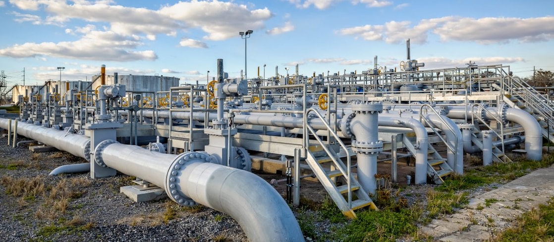 Instalação industrial de gás natural com tubulações metálicas, válvulas e equipamentos de controle em área externa sob céu azul.