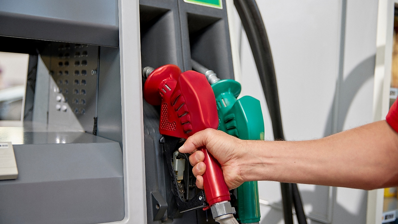 Mão de um frentista segurando bico da bomba de abastecimento