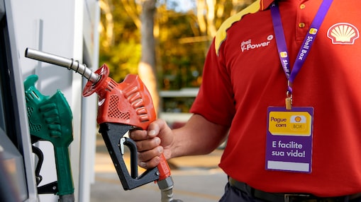 Frentista em frente a bomba de combustível preparando para abastecer um carro