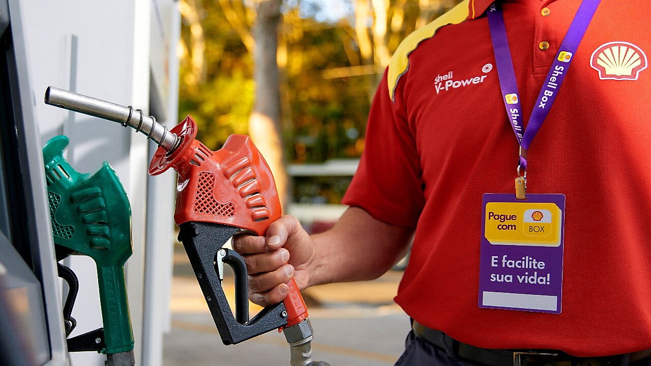 Frentista em frente a bomba de combustível preparando para abastecer um carro