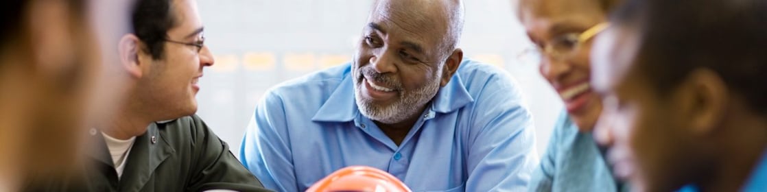 Cinco pessoas conversam ao redor de uma mesa de escritório, em clima de descontração