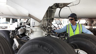 Funcionário visto embaixo de um avião trocando o seu combustível