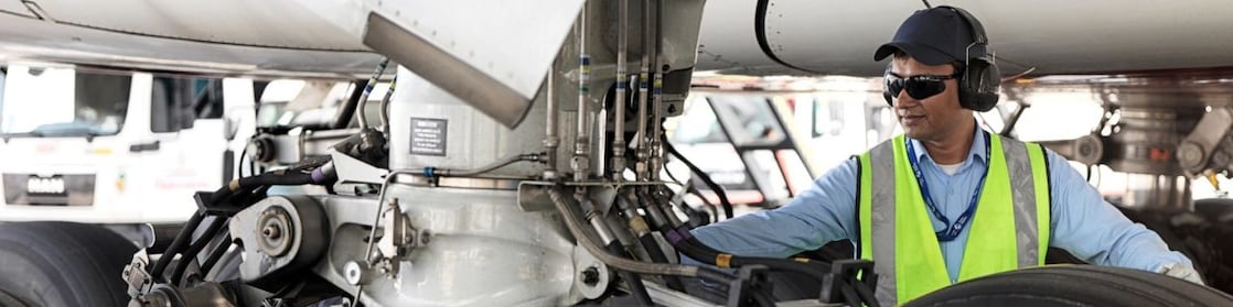 Funcionário visto embaixo de um avião trocando o seu combustível