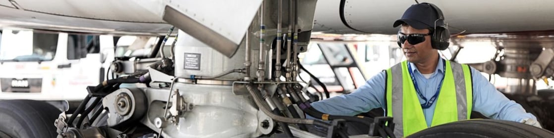 Funcionário visto embaixo de um avião trocando o seu combustível