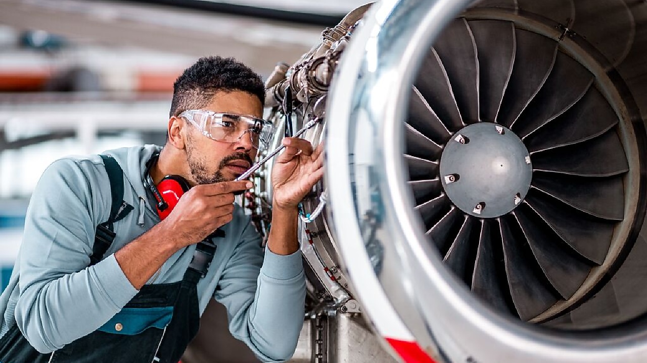 Foto mostra um homem com equipamentos de proteção individual realizando uma vistoria em uma turbina de avião