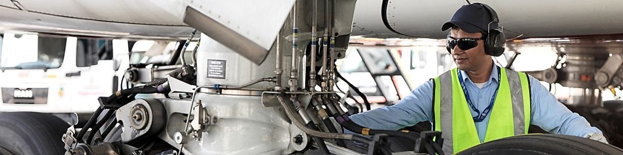 Funcionário visto embaixo de um avião trocando o seu combustível