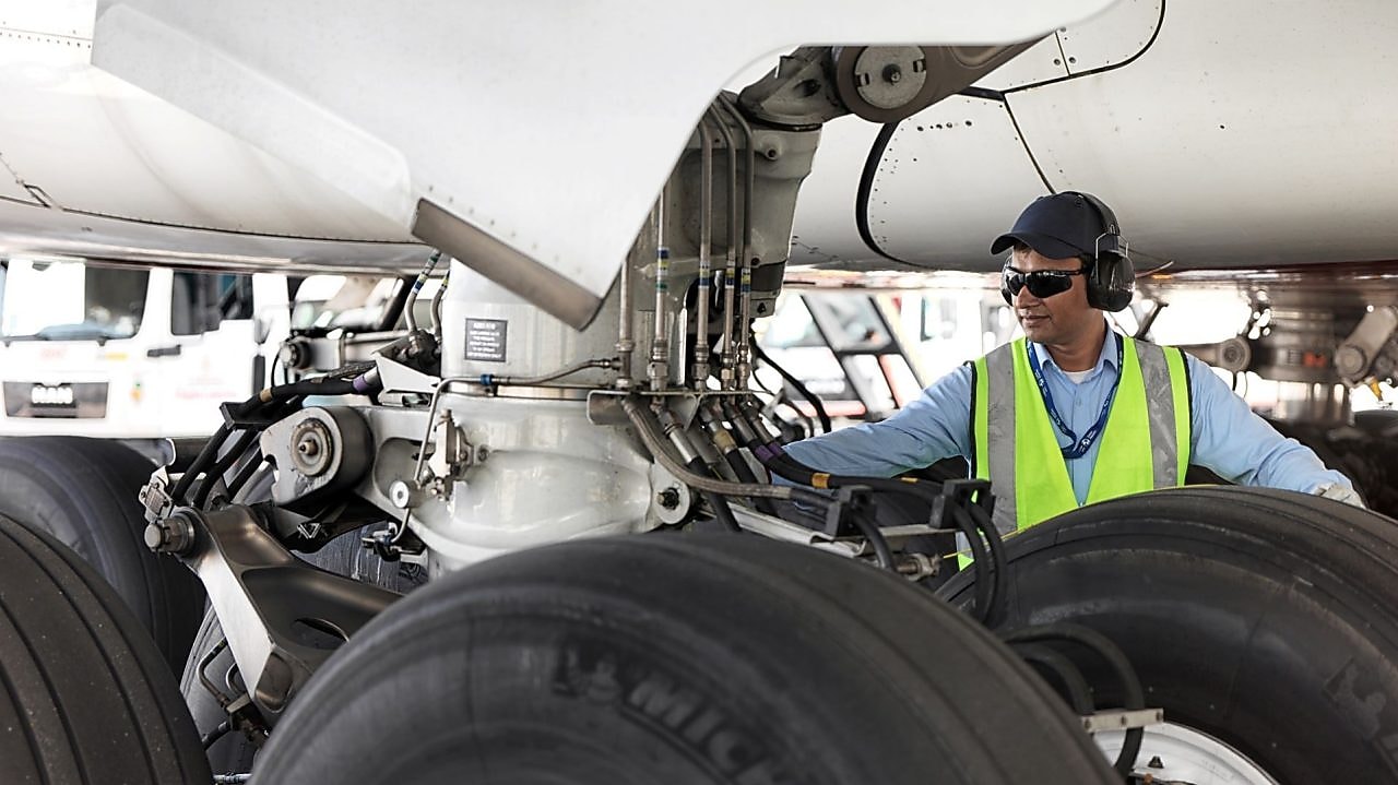 Funcionário visto embaixo de um avião trocando o seu combustível