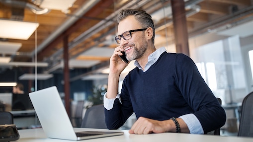 Homem falando ao celular com um laptop à frente