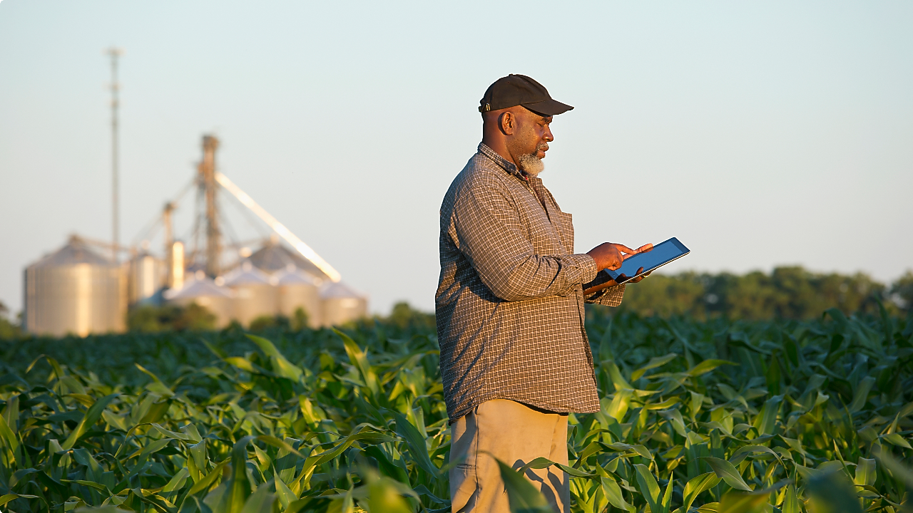 Homem usando um tablet em um campo de plantação com silos ao fundo