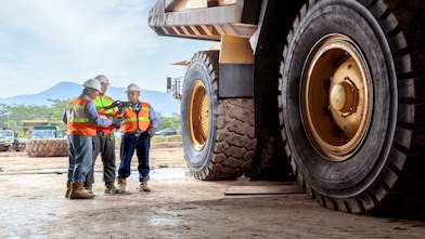 Três pessoas com equipamentos de segurança próximo a um equipamento em uma mineradora
