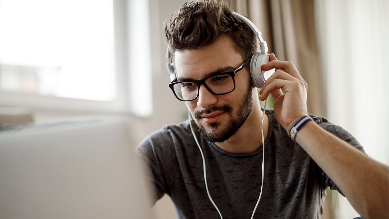 Pessoa sentada em frente a um computador, com webcam posicionada à frente, gravando ou enviando um vídeo. A tela do computador está ligada e a pessoa aparece enquadrada para gravação 