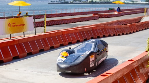 Protótipo de veículo da Shell Eco-marathon em movimento durante a competição no Rio de Janeiro. O carro, de estrutura leve e transparente, com o número 309, percorre a pista cercada por barreiras de segurança vermelhas, com o mar e embarcações ao fundo.