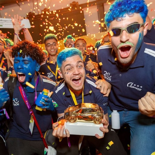 Estudantes comemoram com entusiasmo a vitória na Shell Eco-marathon, segurando troféus dourados em meio a chuva de papel picado, com rostos pintados e expressões de euforia. 