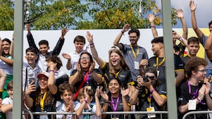 Público formado por estudantes e visitantes vibra nas arquibancadas durante a Shell Eco-marathon, com aplausos, sorrisos e registros com celular e câmera fotográfica. 