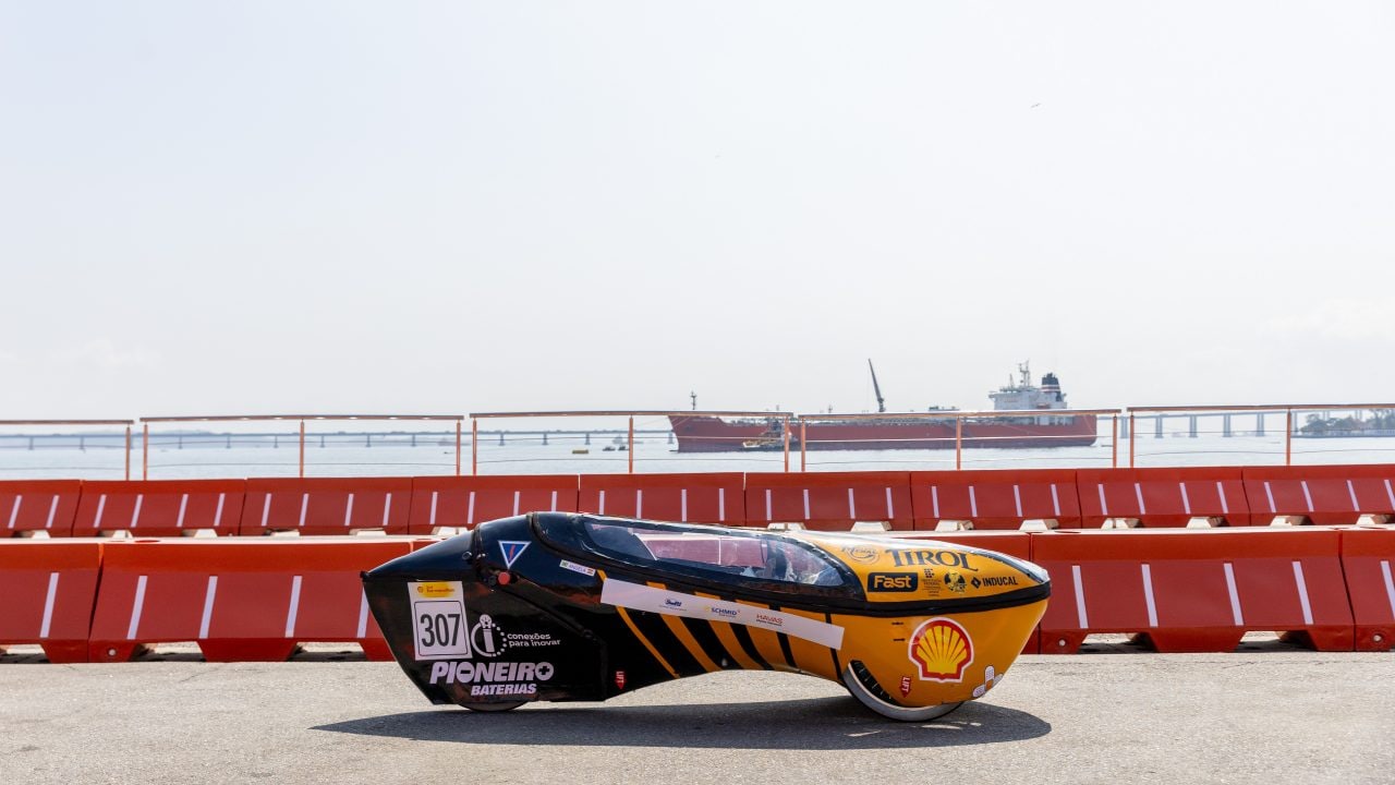 Protótipo número 307 circula na pista com vista para a Baía de Guanabara, durante a Shell Eco-marathon. Ao fundo, navios e a Ponte Rio-Niterói compõem a paisagem. 