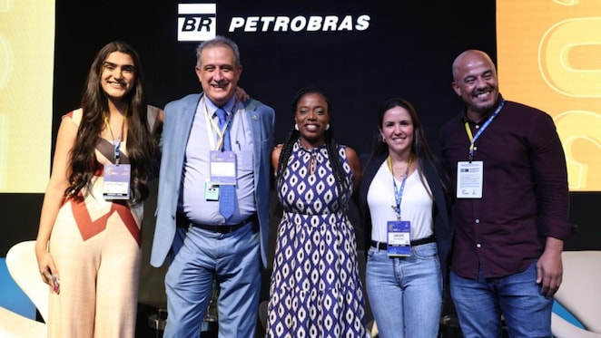 Os cinco palestrantes posam juntos no palco. Da esquerda para a direita, uma mulher jovem com cabelos longos e roupa clara, um homem mais velho de terno azul claro e gravata, uma mulher negra com vestido estampado de azul e branco, outra mulher com blusa branca e jeans, e um homem careca com camisa escura e jeans. Eles estão sorrindo, em frente a um fundo preto com o logotipo da Petrobras.