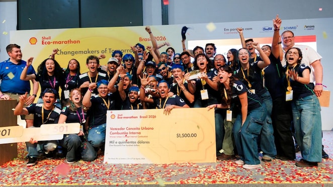 Equipe celebra uma vitória na Shell Eco-marathon Brasil 2026, com integrantes reunidos no palco, erguendo troféus e comemorando em meio a confetes. À frente, o grupo exibe o prêmio de vencedor da categoria Conceito Urbano – Combustão Interna.