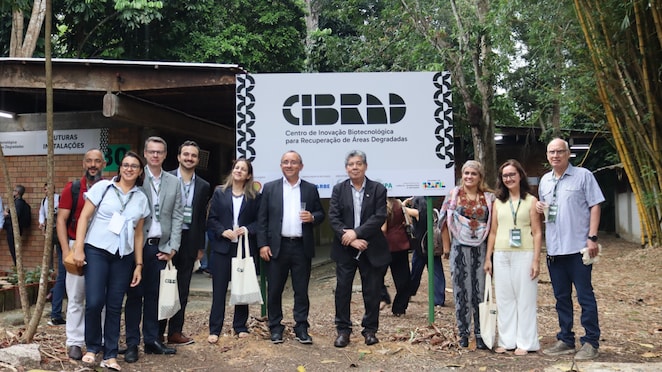 Grupo de pessoas posando ao ar livre em frente a uma placa com o texto ‘Cibrad – Centro de Inovação Biotecnológica para Recuperação de Áreas Degradadas’, em área arborizada, durante evento institucional.