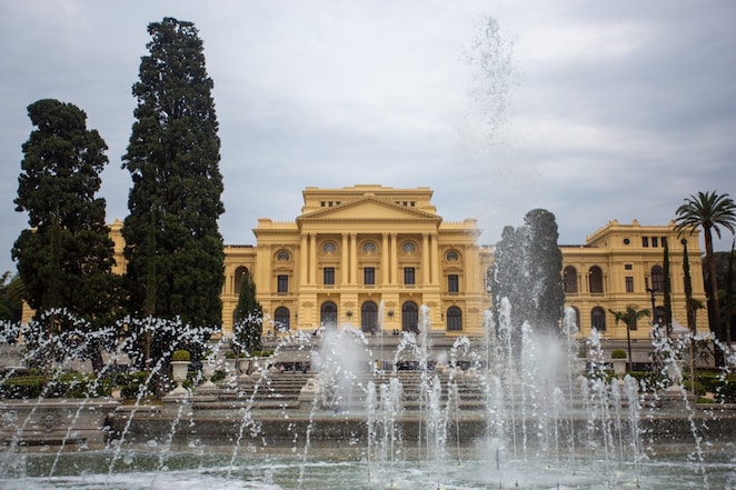 Fachada do Museu do Ipiranga, em São Paulo, com fonte de água em primeiro plano e jardins ao redor