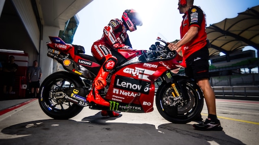 Piloto da equipe Ducati Corse saindo de motocicleta do box e cumprimentando equipe