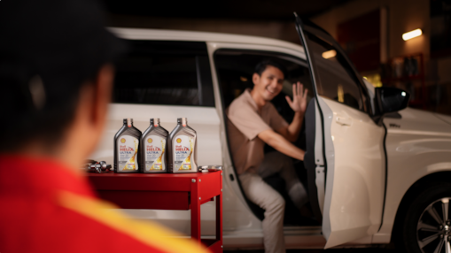 Homem saindo de um carro acenando para frentista e, ao lado, mesa com lubrificante Shell Helix