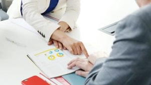 Mão apontando informação em folheto. Durante reunião entre duas pessoas, uma delas aponta para informação presente em folheto.