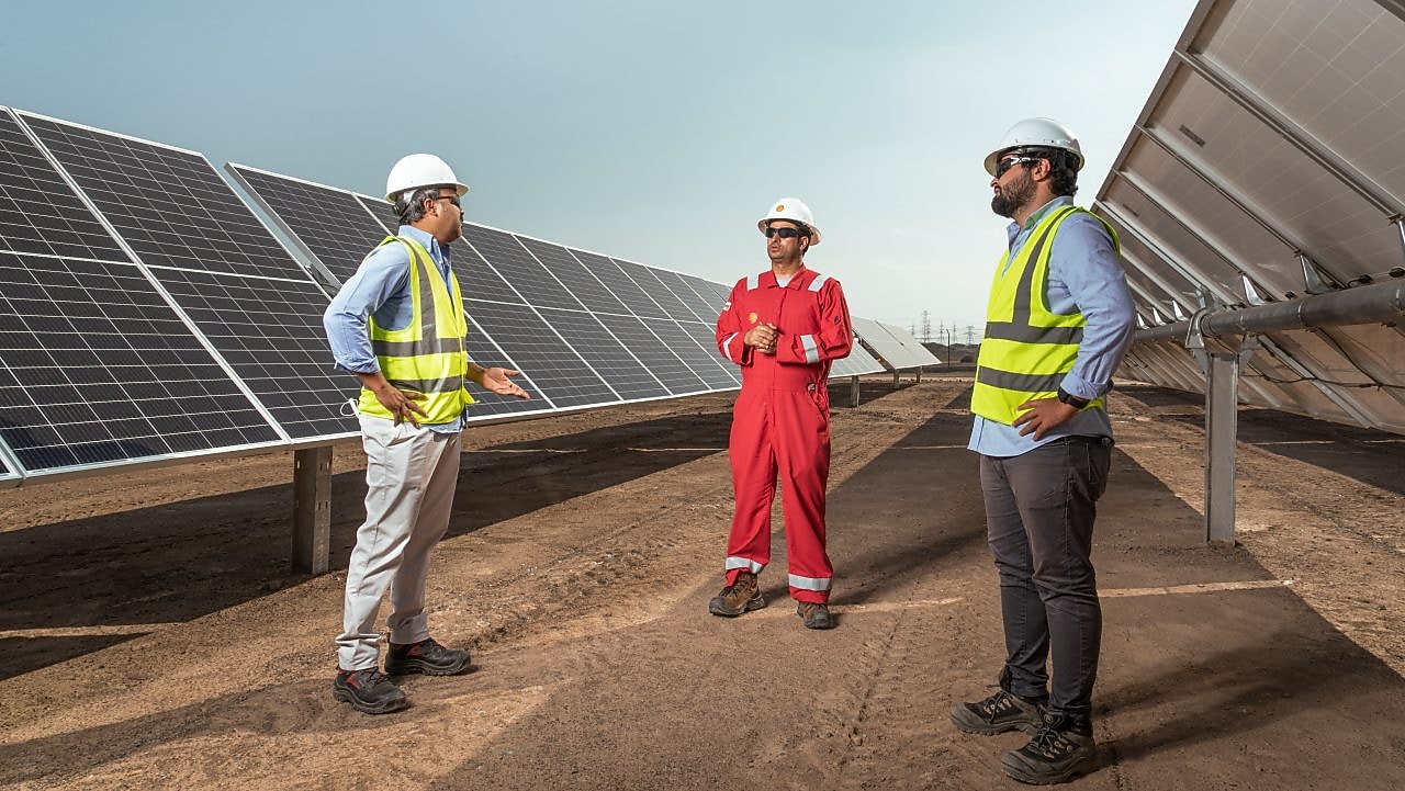 Três homens conversando em um corredor com placas solares em volta