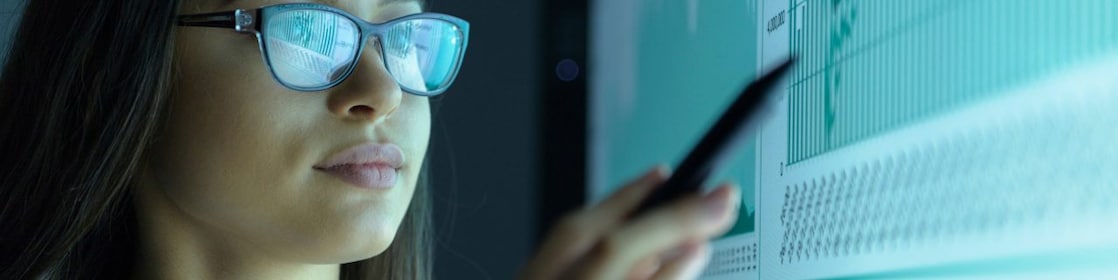 Jovem mulher de óculos aponta para uma tela exibindo alguns gráficos