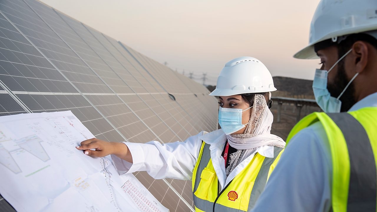 Na imagem, vemos um homem e uma mulher no canto direito analizando papéis apoiados sobre placas solares.