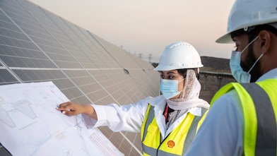 Na imagem, vemos um homem e uma mulher no canto direito analizando papéis apoiados sobre placas solares.