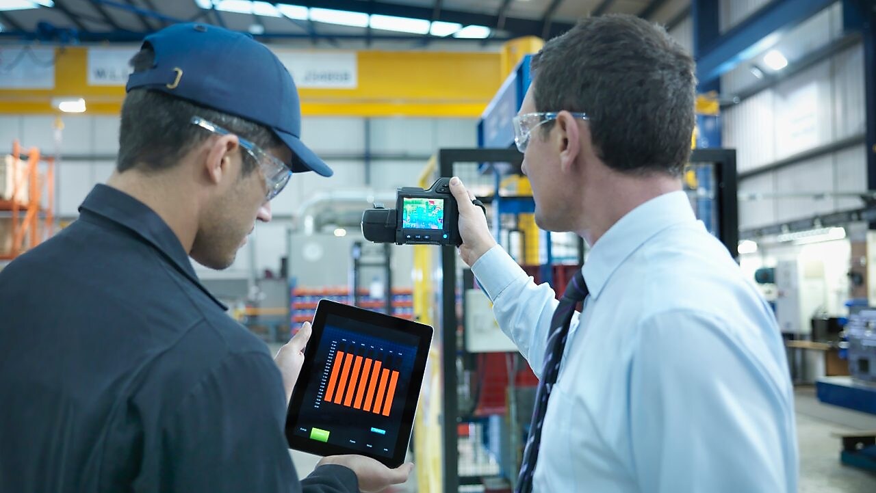 Colaboradores usando tablet digital e câmera infravermelha para verificar o uso de energia na fábrica