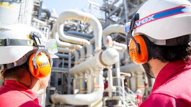 Dupla de operadores em primeiro plano observando tubulações de gás natural