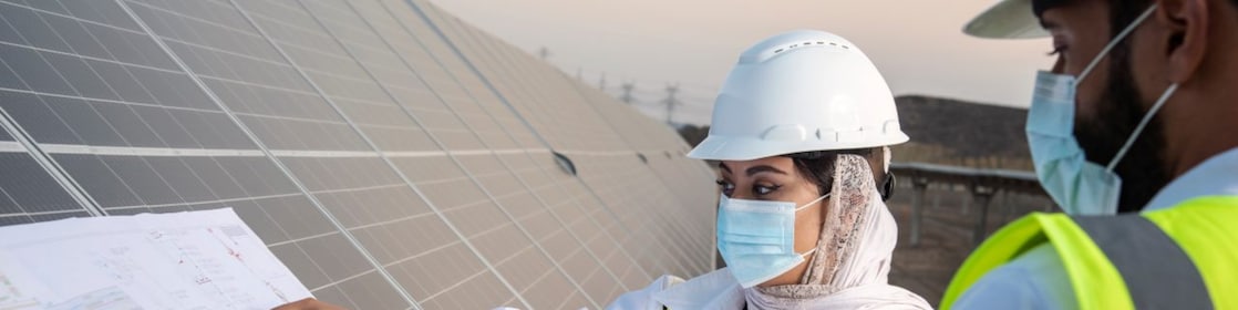 Na imagem, vemos um homem e uma mulher no canto direito analizando papéis apoiados sobre placas solares.