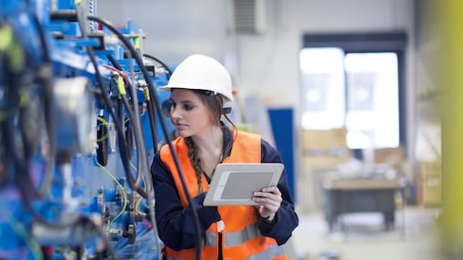 Técnica no salão da fábrica inspecionando máquina com tablet digital