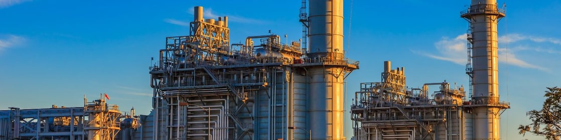 Na imagem, temos uma vista de uma planta para extração de gás natural, com uma pequena vegetação na frente da construção.