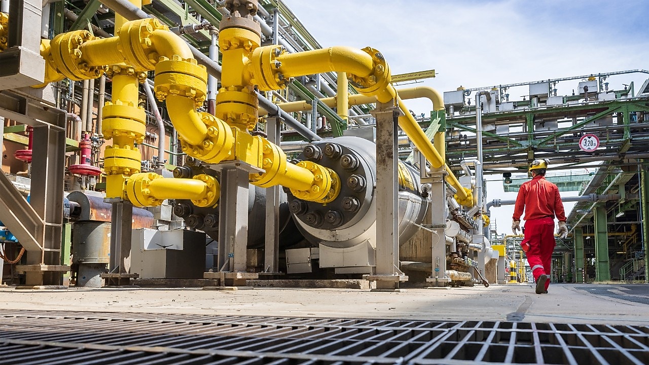 Uma cena industrial ao ar livre com tubulações amarelas brilhantes conectadas a grandes máquinas.