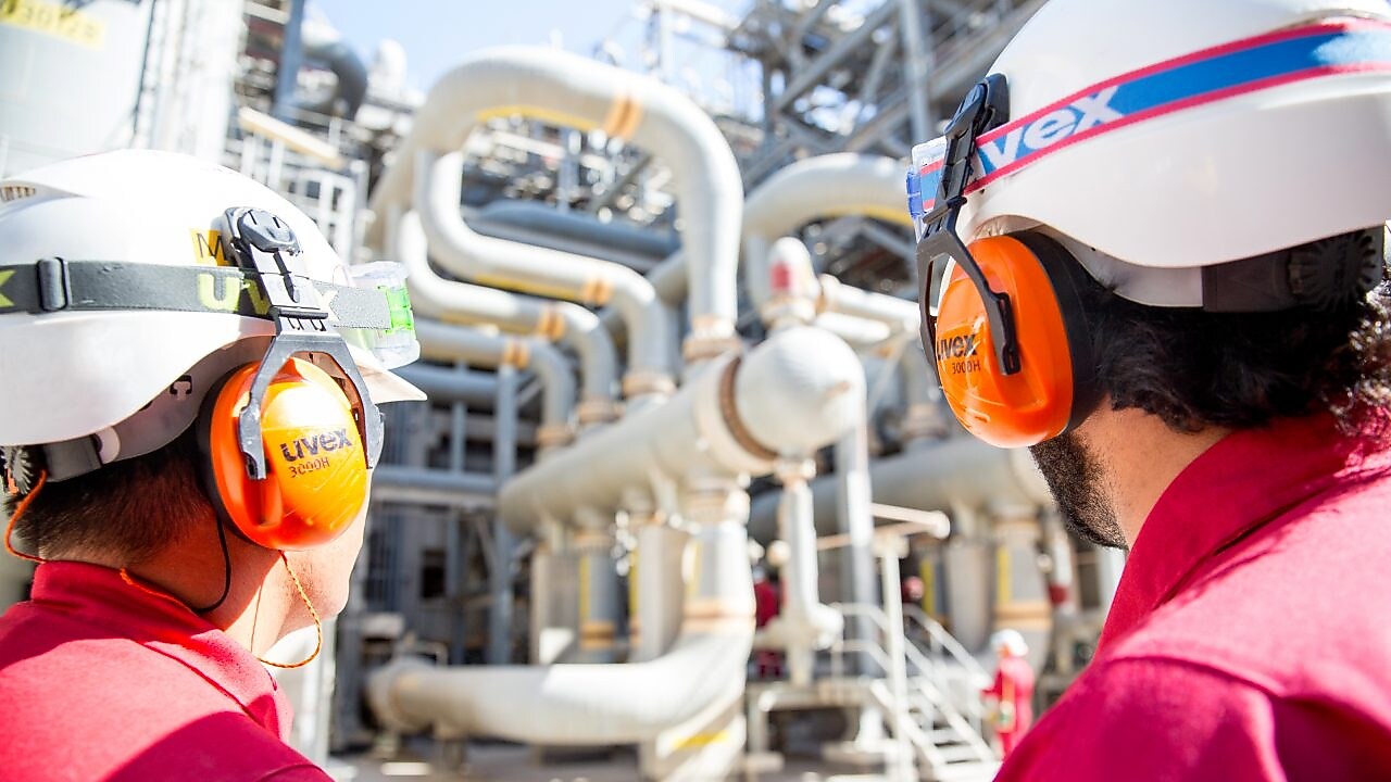 Dupla de operadores em primeiro plano observando tubulações de gás natural