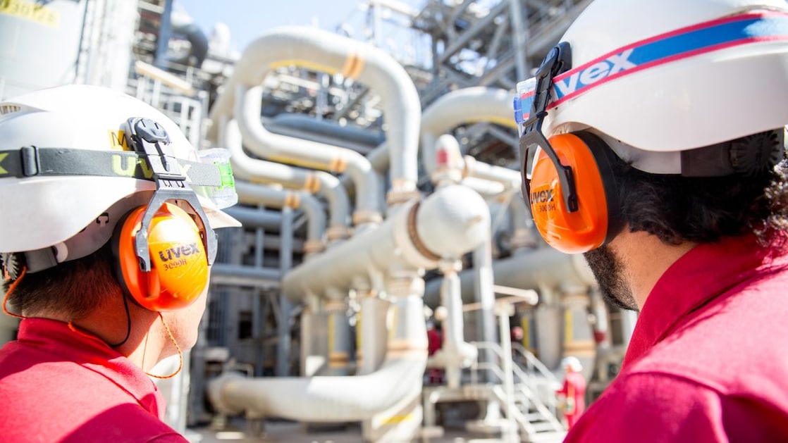 Dupla de operadores em primeiro plano observando tubulações de gás natural