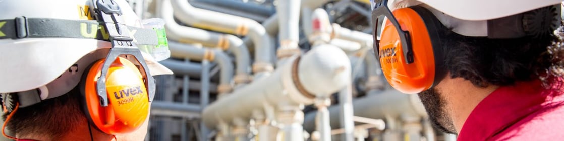 Dupla de operadores em primeiro plano observando tubulações de gás natural